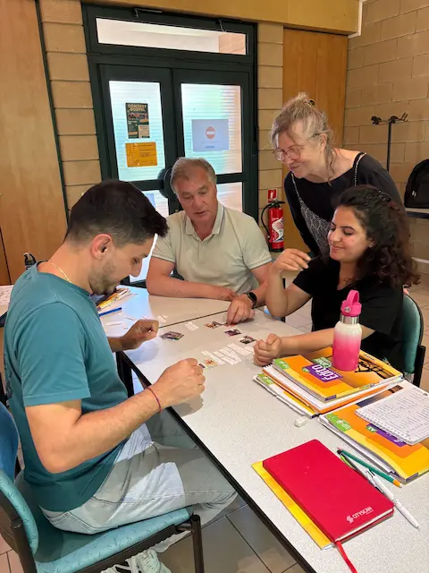 Petit groupe d'apprenants et de bénévoles rassemblés autour d'une table pendant un jeu pédagogique de français.