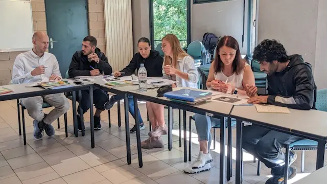 Accompagnement sur-mesure : élèves et formateurs assit en demi-cercle autour d'une table lors d'un cours de Français Langue Étrangère.
