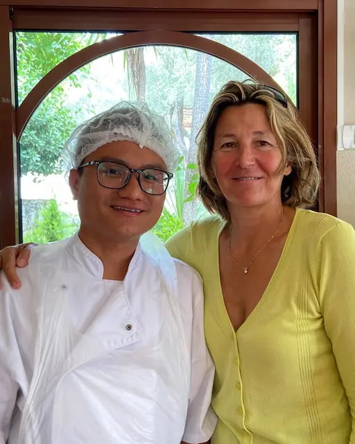 Un participant en tenue de cuisine professionnelle posant aux côtés d'une accompagnatrice de l'association.